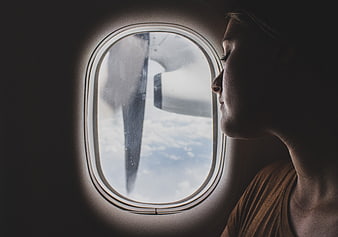 Woman looking out airplane window at clouds and wing