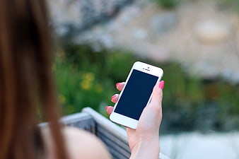 Woman holding white smartphone with blank screen outdoors