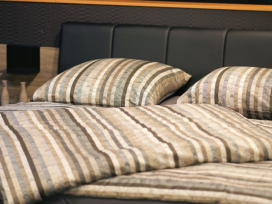 Striped Bedding Set On Black Leather Headboard In Modern Hotel Bedroom