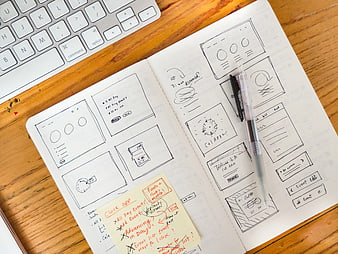 Hand-drawn UI wireframes in sketchbook on wooden desk