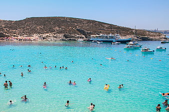 Crowded turquoise beach with boats and swimmers