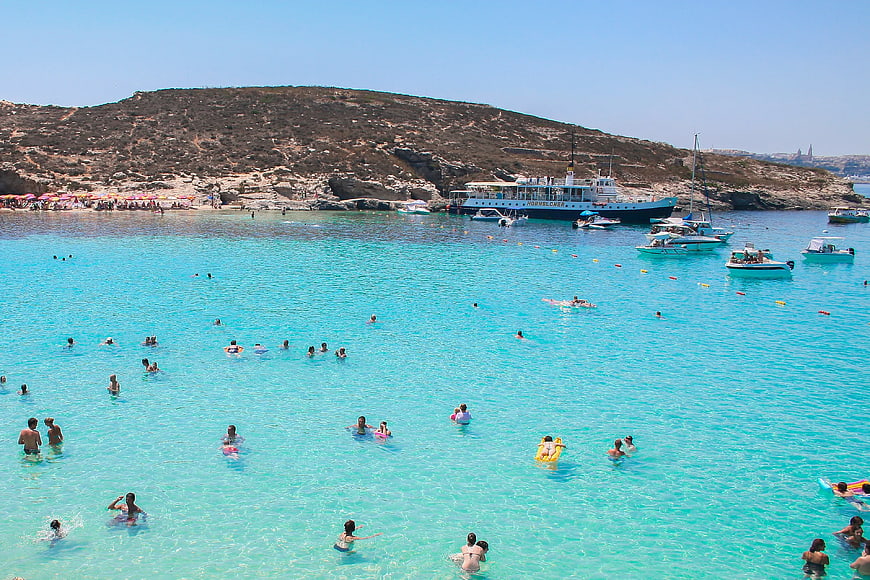 Crowded turquoise beach with boats and swimmers