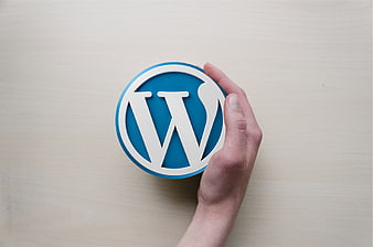 Hand holding blue WordPress logo on wooden background