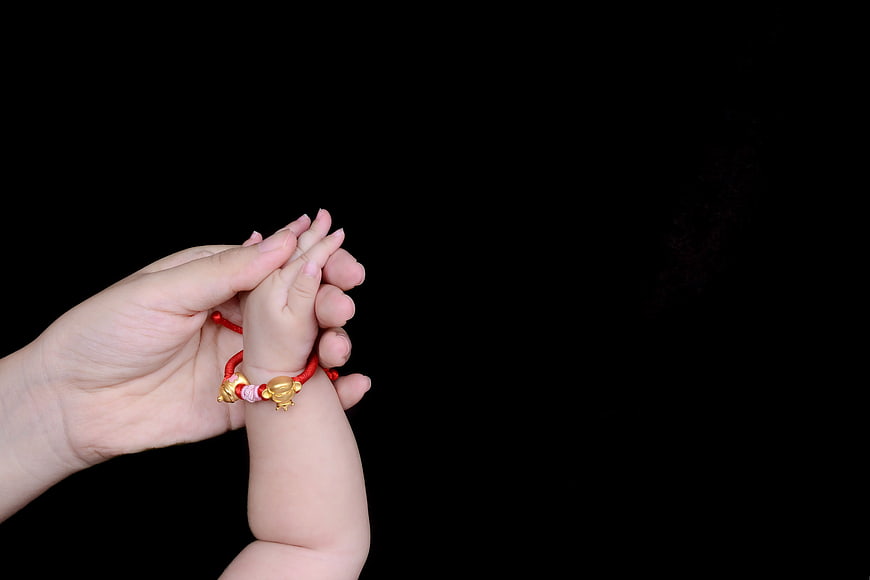 Adult Hand Holding Baby Hand with Red Bracelet