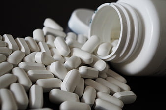 White pills spilling from bottle on black background