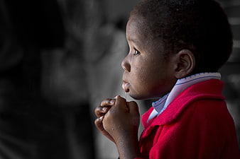 African child in red coat eating lollipop in profile