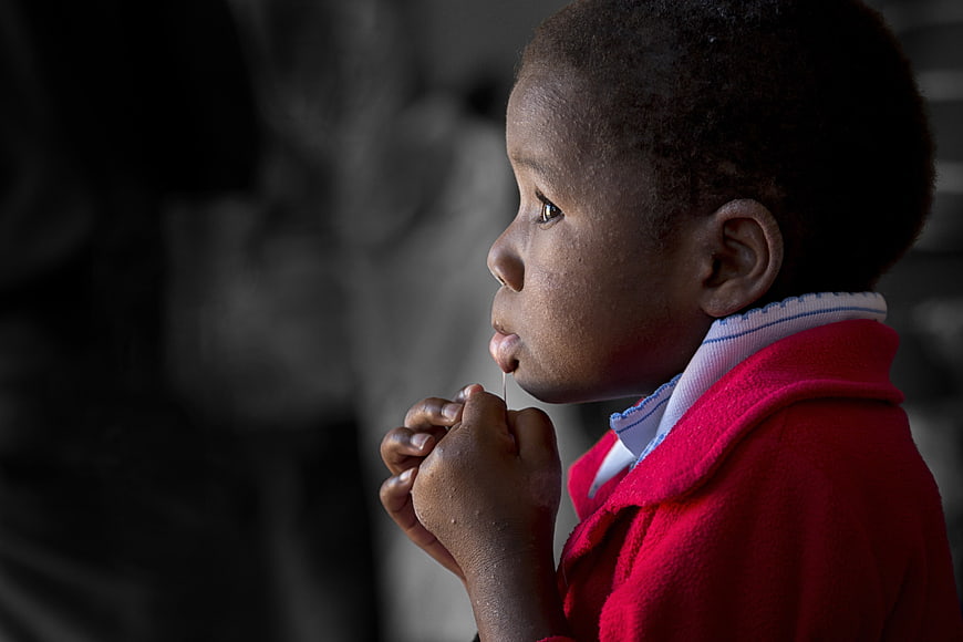 African child in red coat eating lollipop in profile