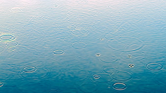 Raindrops creating ripples on a calm blue water surface