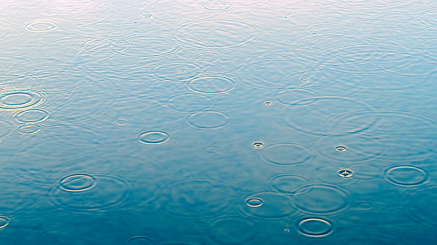 Raindrops creating ripples on a calm blue water surface