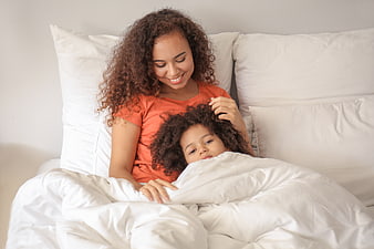 Mother and daughter cuddling in bed with white linens
