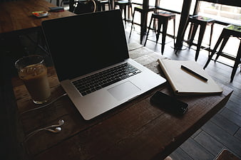 Laptop, notebook, and iced coffee on rustic wooden table in cafe