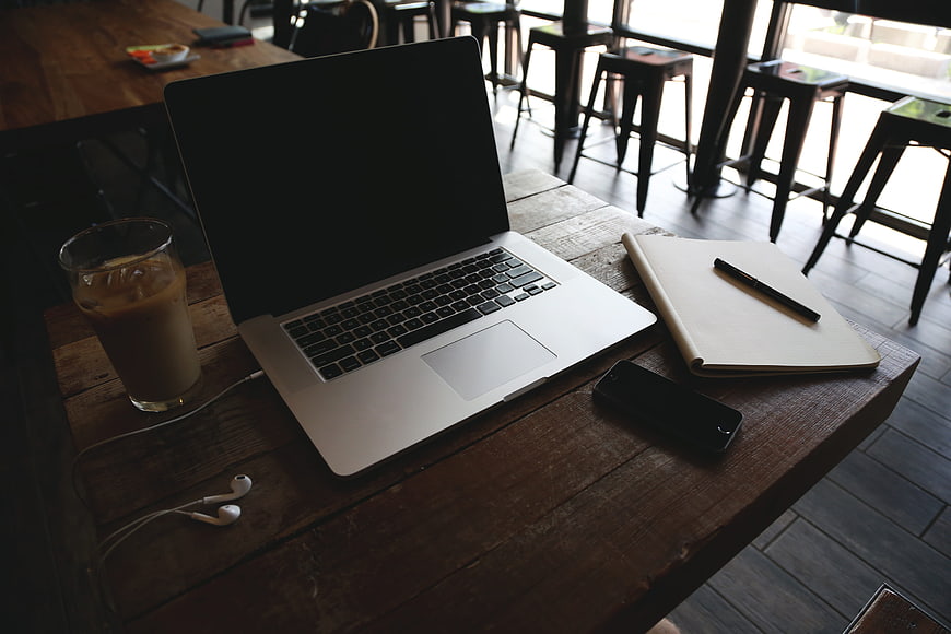 Laptop, notebook, and iced coffee on rustic wooden table in cafe