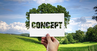 Hand holding card with concept word cutout against green landscape