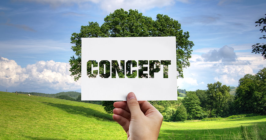 Hand holding card with concept word cutout against green landscape