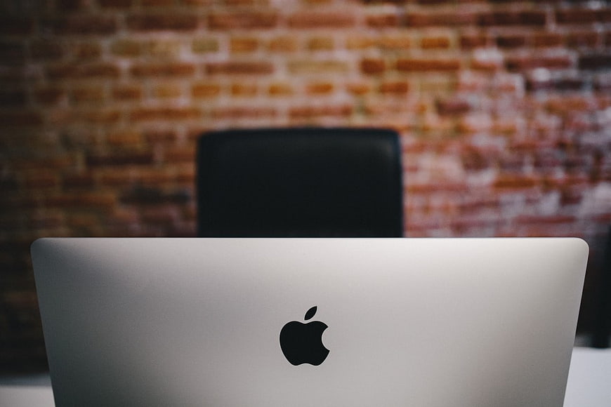 Silver MacBook Laptop on Desk with Blurred Brick Wall Background