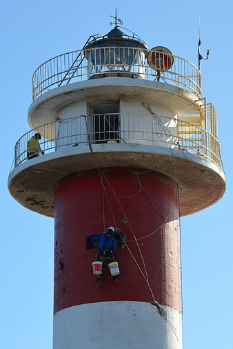 Worker repainting red lighthouse exterior with ropes