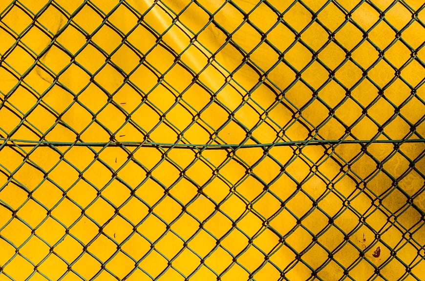 Green chain link fence against vibrant yellow background texture