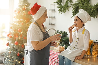 Grandmother and granddaughter baking cookies in kitchen with Christmas tree