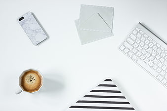 Minimalist white workspace with coffee, keyboard, and smartphone