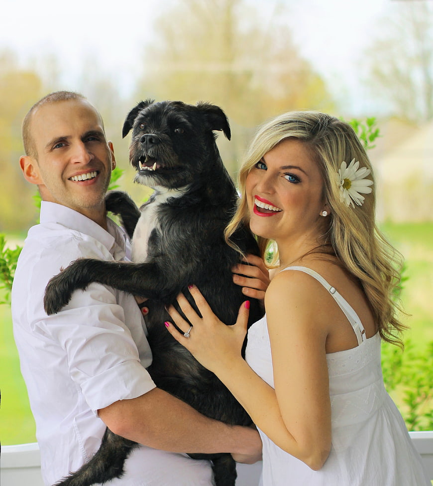 Happy couple holding black dog outdoors in white wedding attire