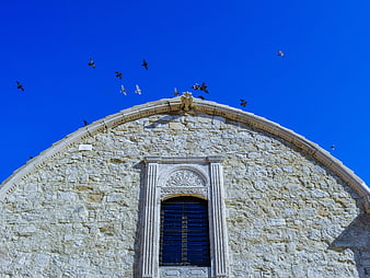 Stone church facade with flying pigeons against blue sky
