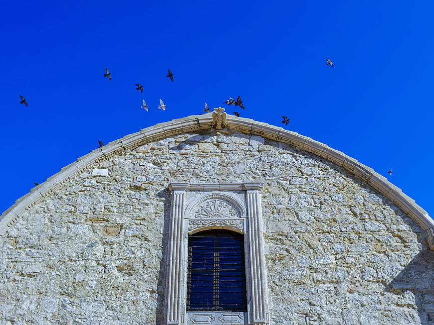 Stone church facade with flying pigeons against blue sky