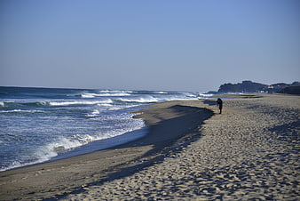Lone figure walking on sandy beach with ocean waves
