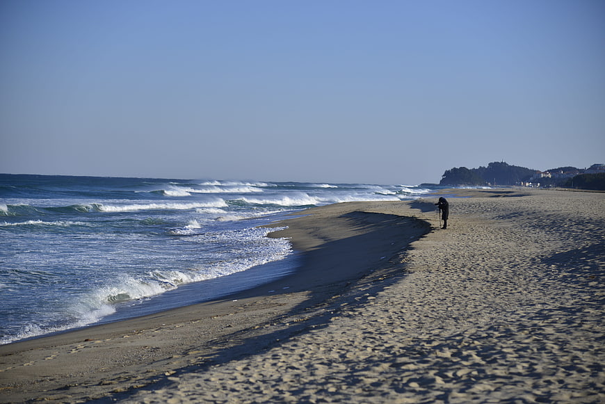 Lone figure walking on sandy beach with ocean waves