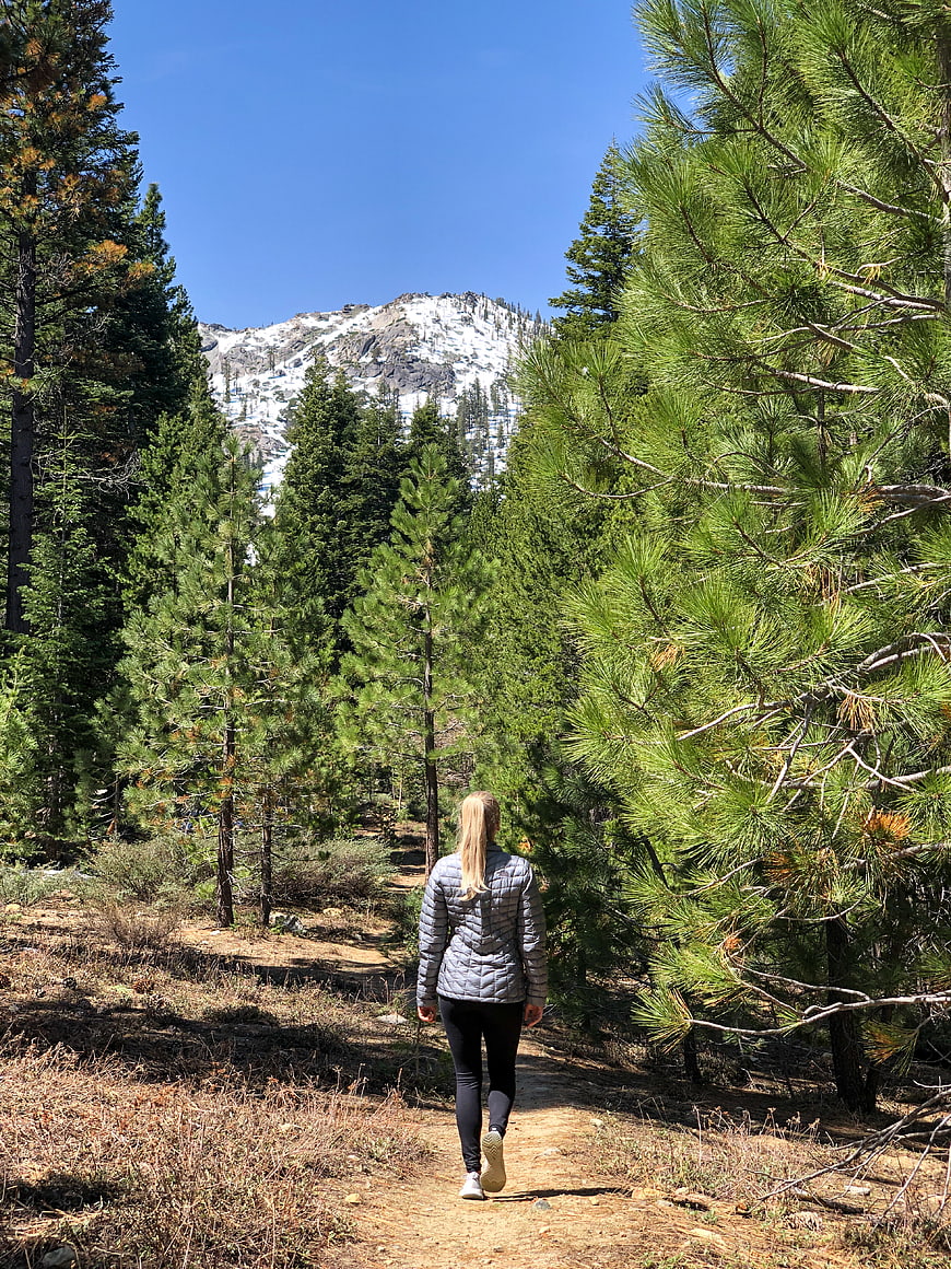 Woman hiking on forest trail with snow-capped mountain background