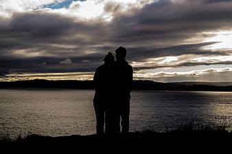 Silhouette of a couple standing by a lake at sunset