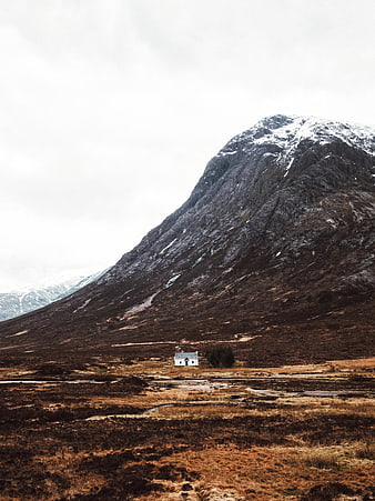 Solitary white cottage at the base of a rugged mountain