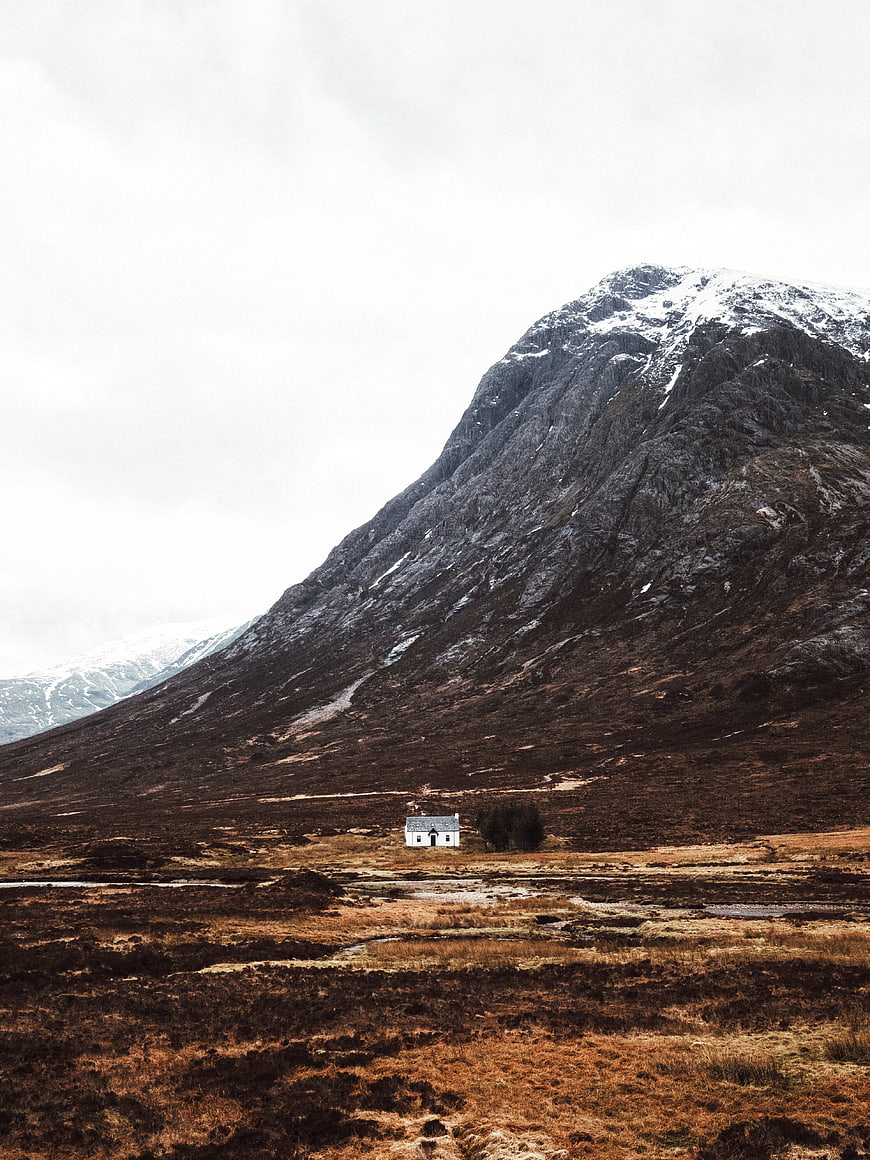 Solitary white cottage at the base of a rugged mountain