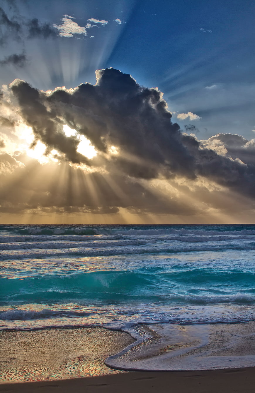 Dramatic Sun Rays Breaking Through Clouds Over Turquoise Ocean Waves
