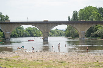 People swimming and playing under stone arch bridge in summer