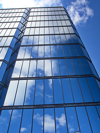 Low angle view of modern glass skyscraper reflecting blue sky