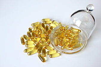 Yellow Fish Oil Capsules Spilled from Glass Jar on White