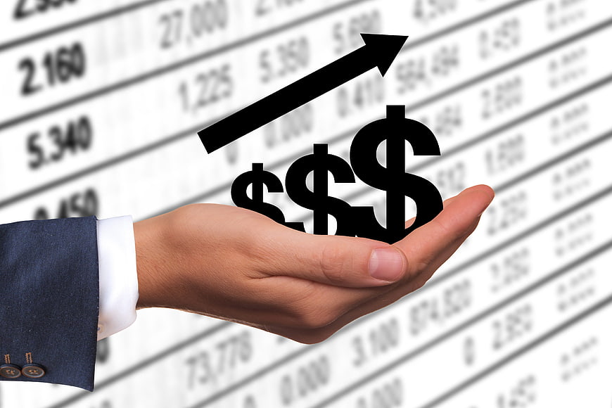 Hand holding dollar signs and growth arrow over financial data