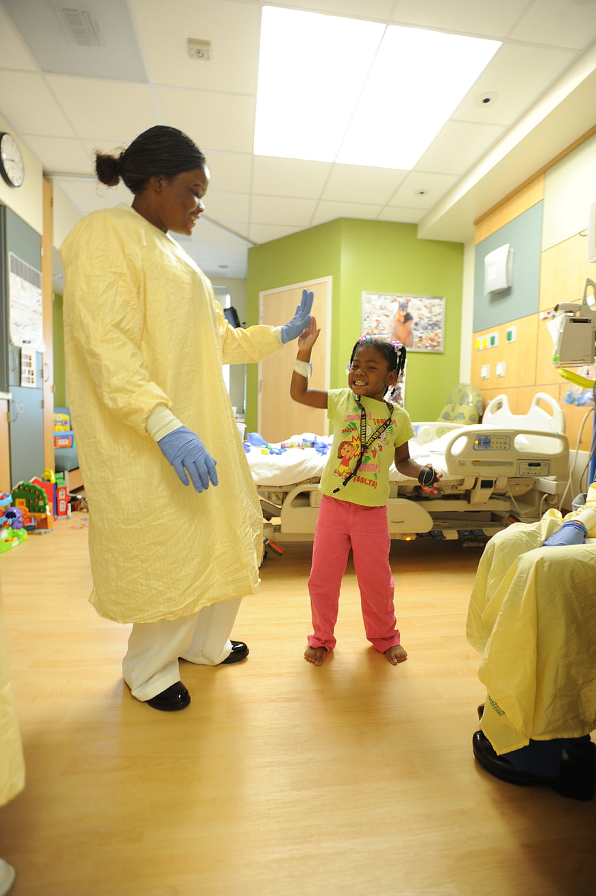 Nurse high-fiving young girl in pediatric hospital room