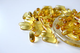 Yellow Fish Oil Capsules Spilling from Glass Bowl