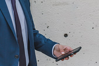 Businessman in Blue Suit Holding Smartphone Against Wall