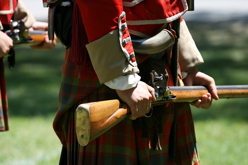 Historical reenactor in red tartan kilt holding musket