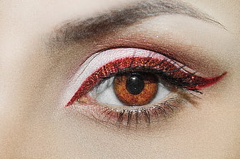 Close-up of eye with red glitter makeup and brown iris