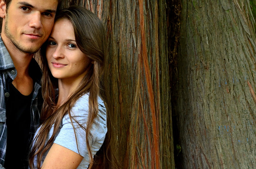 Young couple leaning against tree trunk outdoors