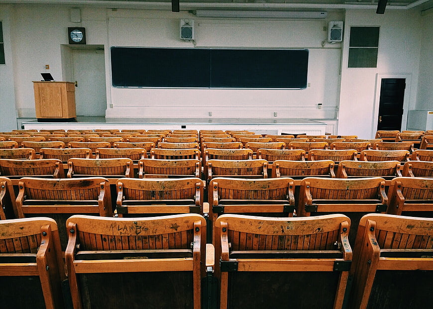 Empty wooden lecture hall with rows of chairs and blackboard