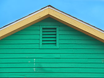 Green wooden house gable with yellow trim against blue sky