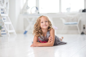 Cute little girl lying on white floor in bright room