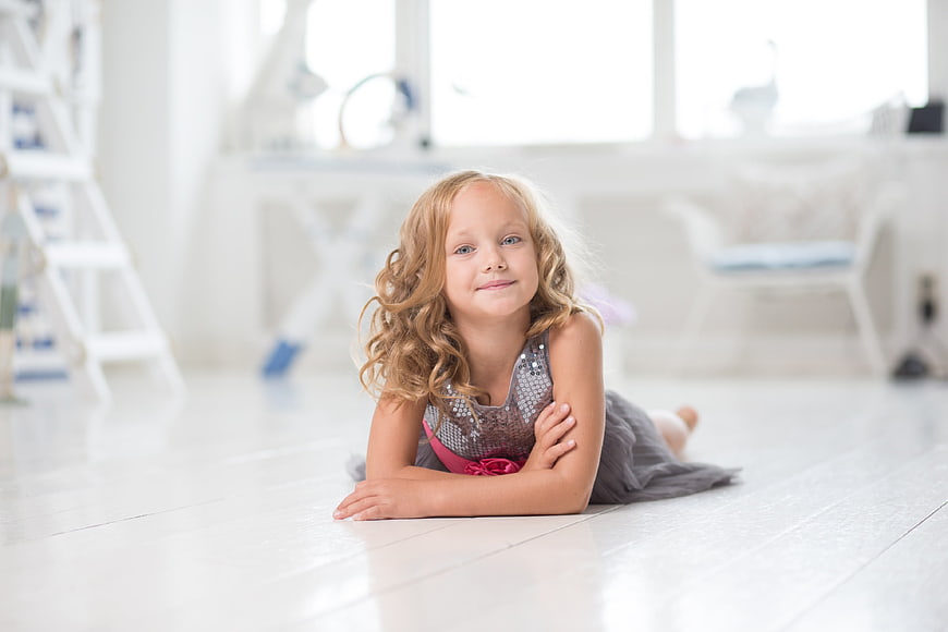 Cute little girl lying on white floor in bright room