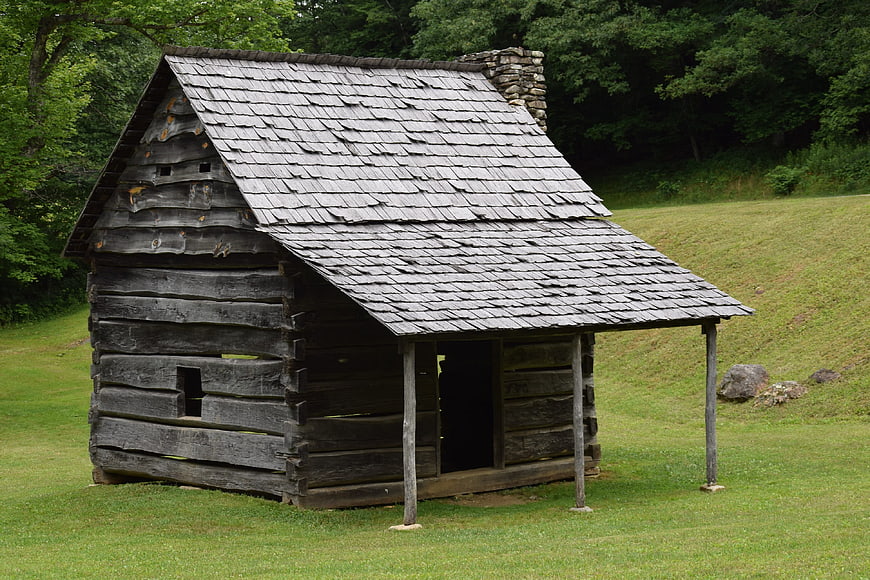 Historic rustic log cabin with weathered wood shingles in a green field