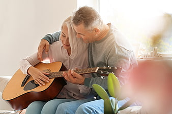 Senior couple playing acoustic guitar together on sofa