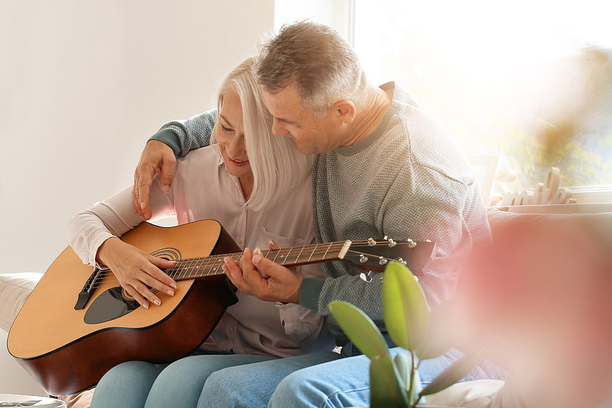 Senior couple playing acoustic guitar together on sofa